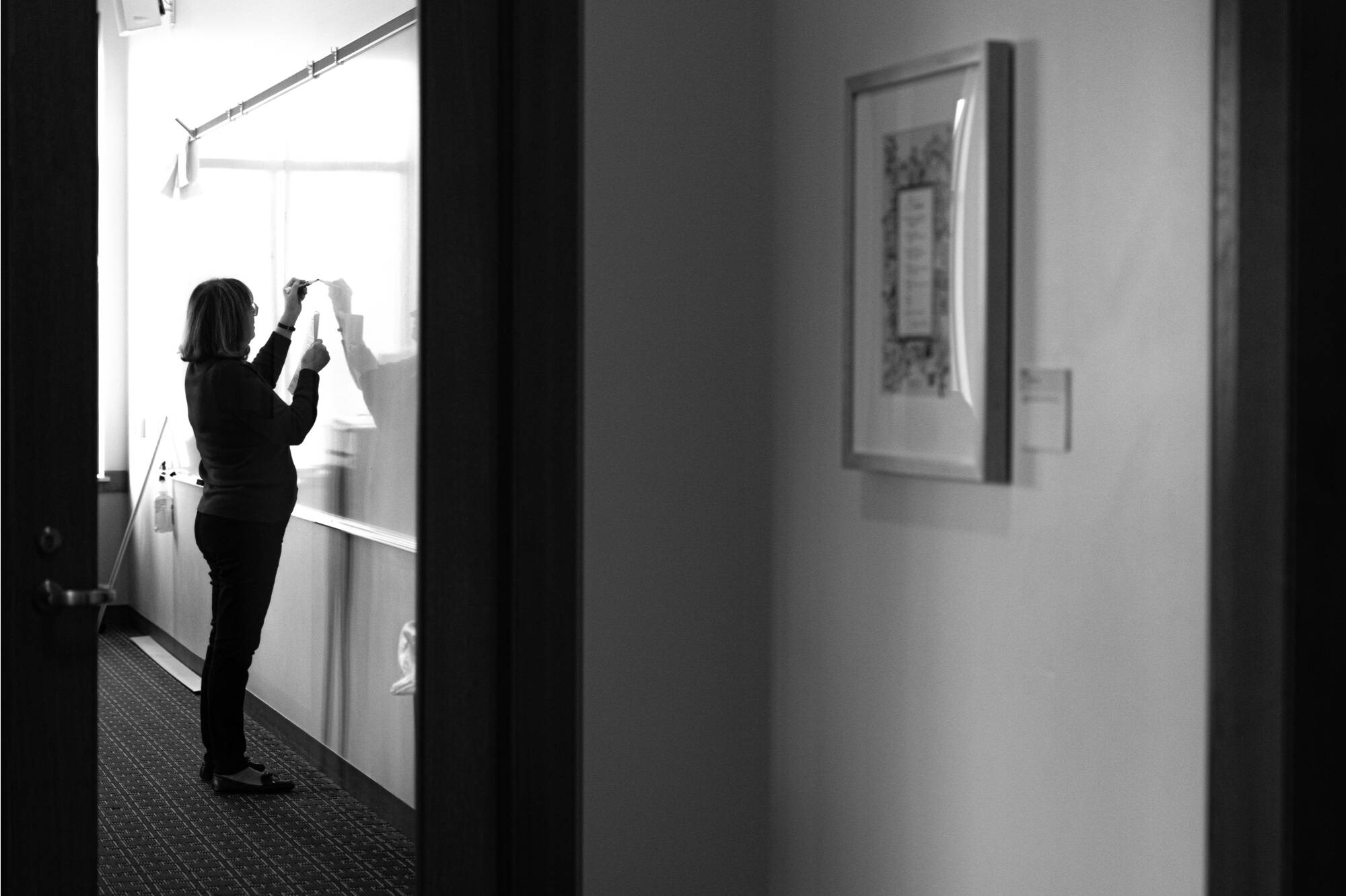 A hallway view of a professor writing on a classroom whiteboard